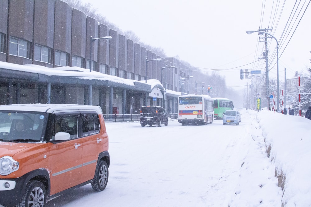 a small orange car driving down a snow covered street