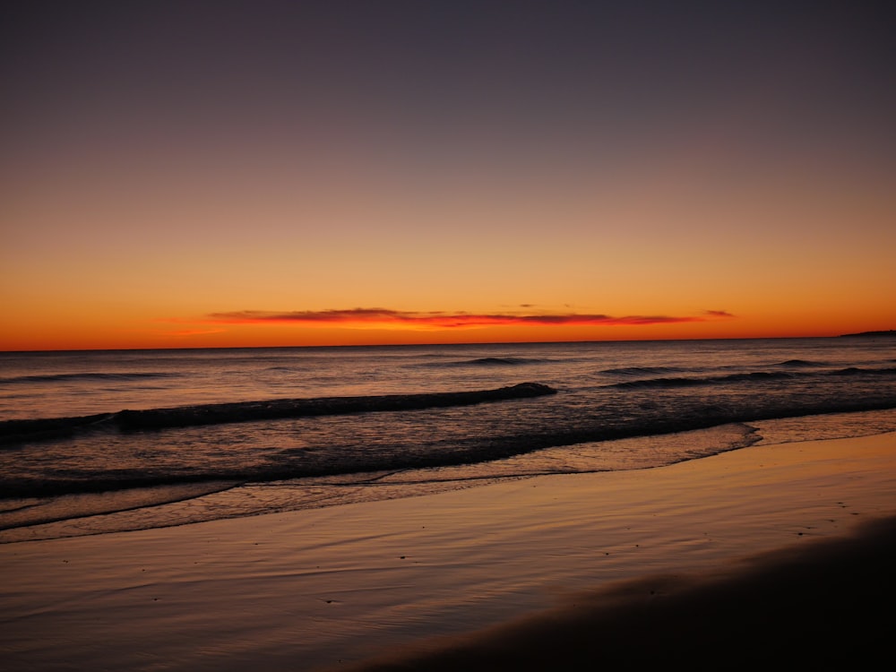 the sun is setting over the ocean on the beach