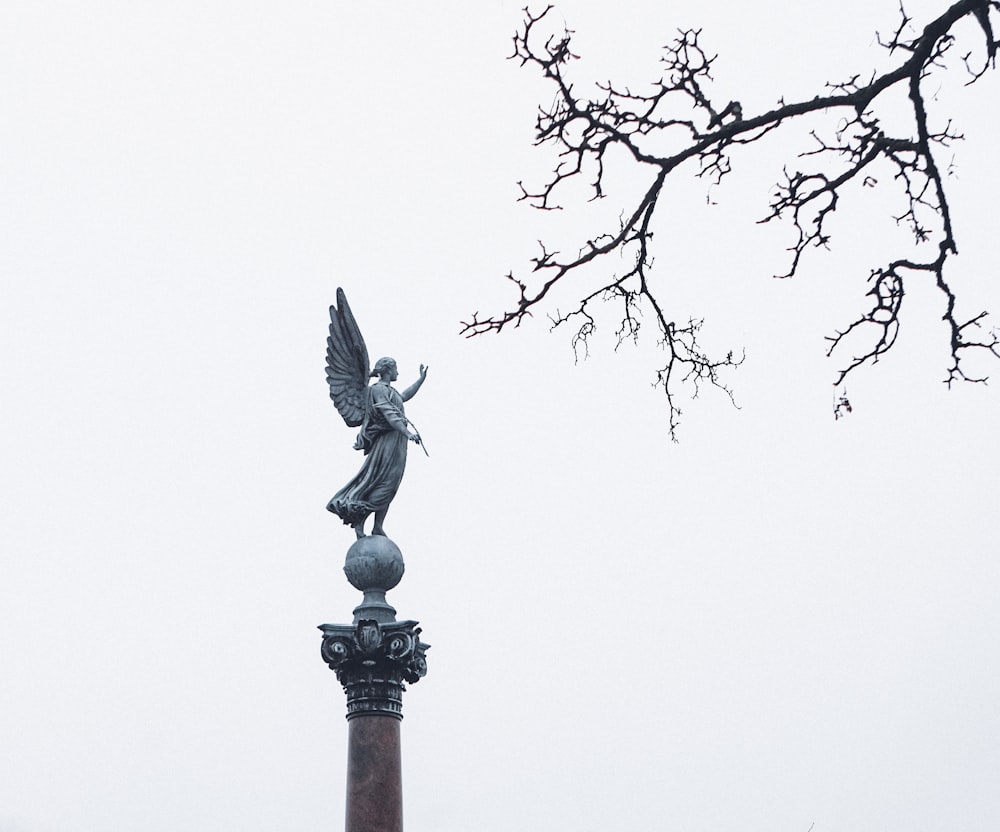 a statue on top of a pillar with a tree in the background