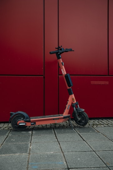 an orange scooter parked in front of a red wall