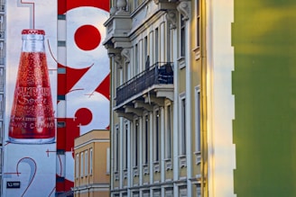A large mural on the side of a building features a Campari Soda bottle prominently alongside bold numbers in a graphic design. The scene includes classic architectural buildings with a modern advertisement.