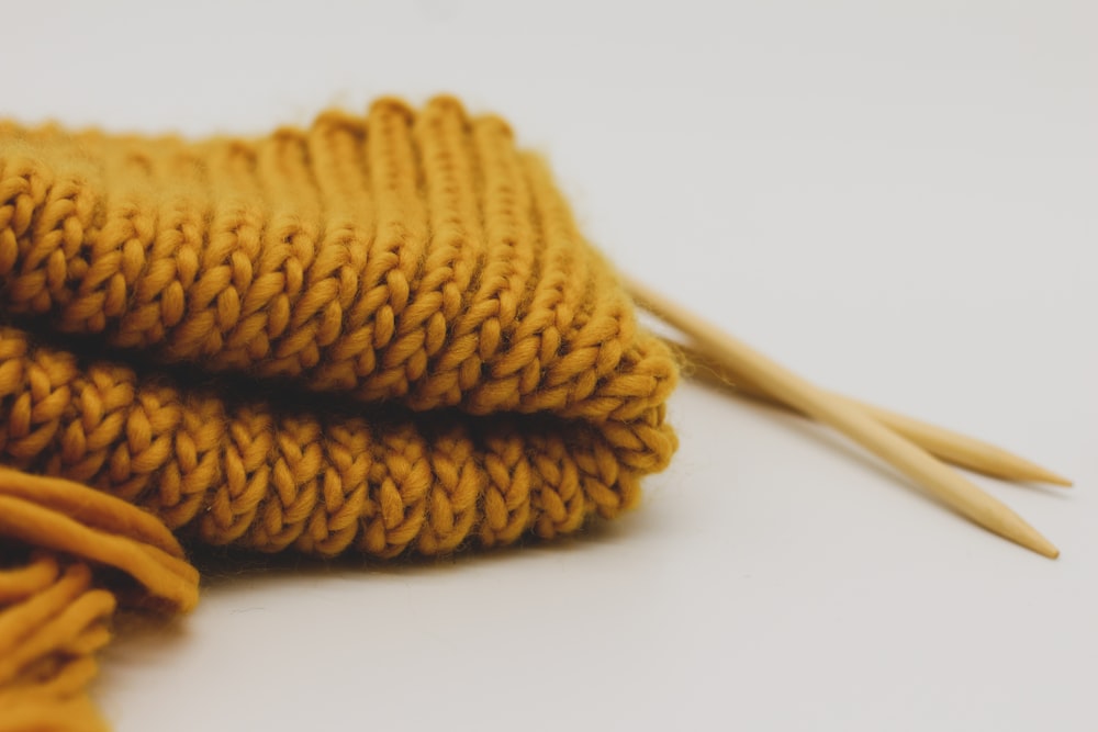 une paire d’aiguilles à tricoter à côté d’un pull jaune