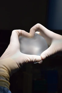 a person in white gloves holding a heart shaped object
