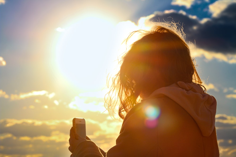 a person holding a cell phone in front of the sun