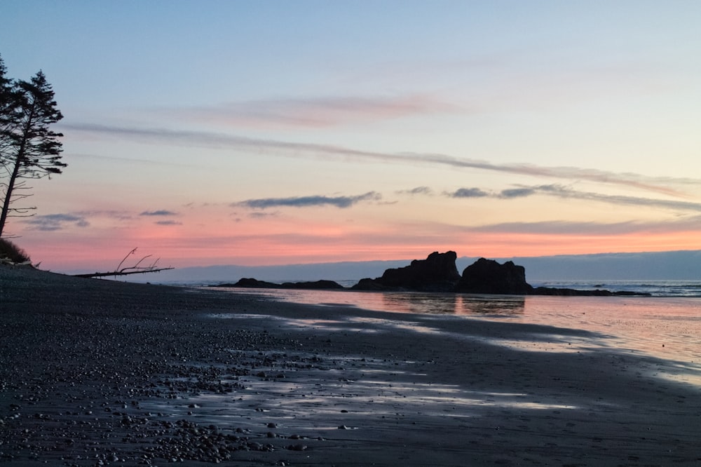 a beach at sunset with a few rocks in the water