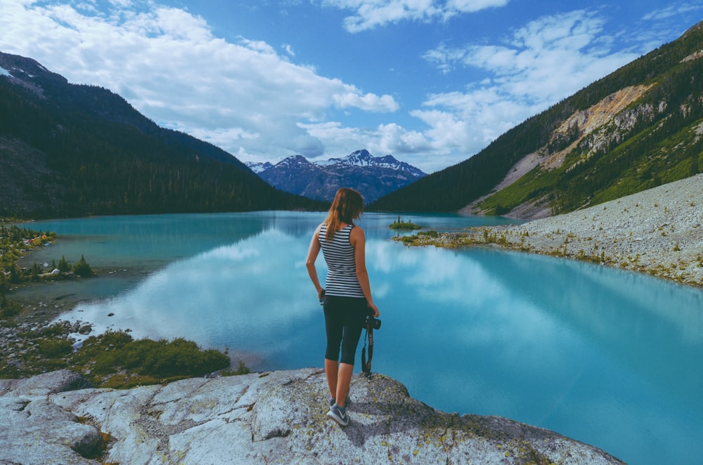 a woman standing on top of a rock next to a lake