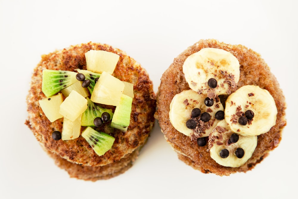 two pancakes with bananas, kiwis, and raisins on them