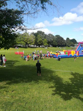 Wide inflatable obstacle course set up in a sunny outdoor park with kids running.