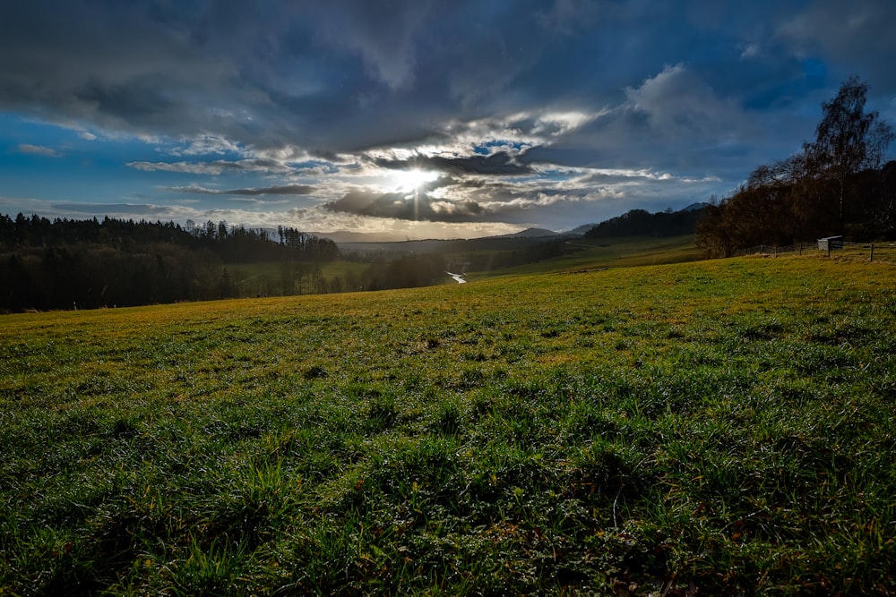 the sun is shining through the clouds over a grassy field