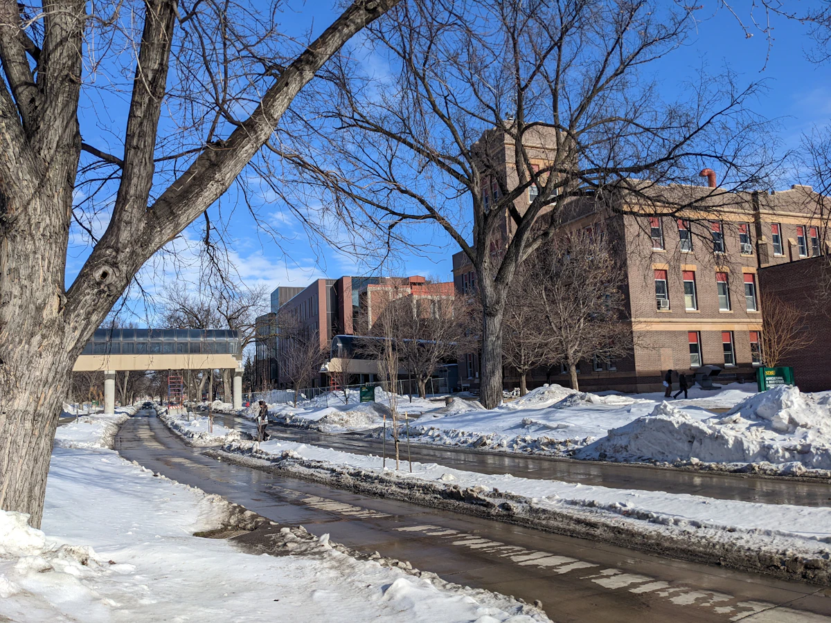Snow beside a cleared road and brick buildings at North Dakota State University in Fargo