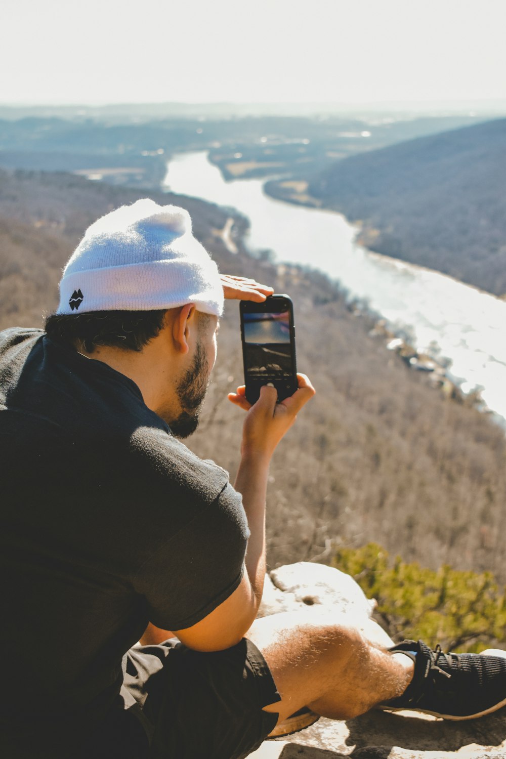 a man sitting on a rock taking a picture of a river