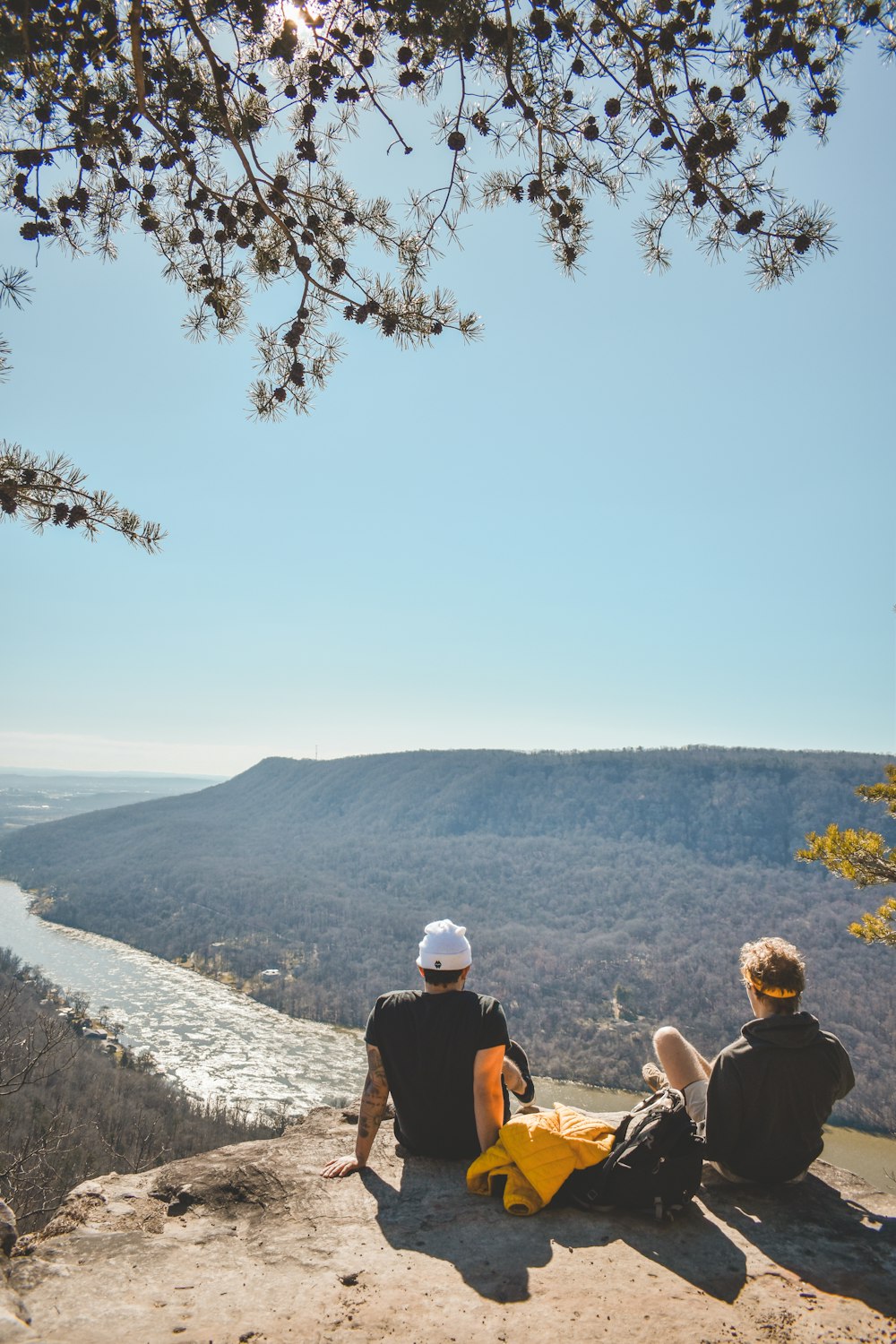 two people sitting on a rock overlooking a valley