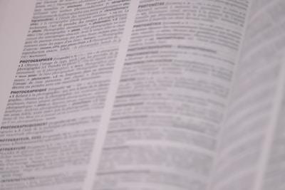 A bilingual dictionary open on a desk beside a laptop showing French and English text.