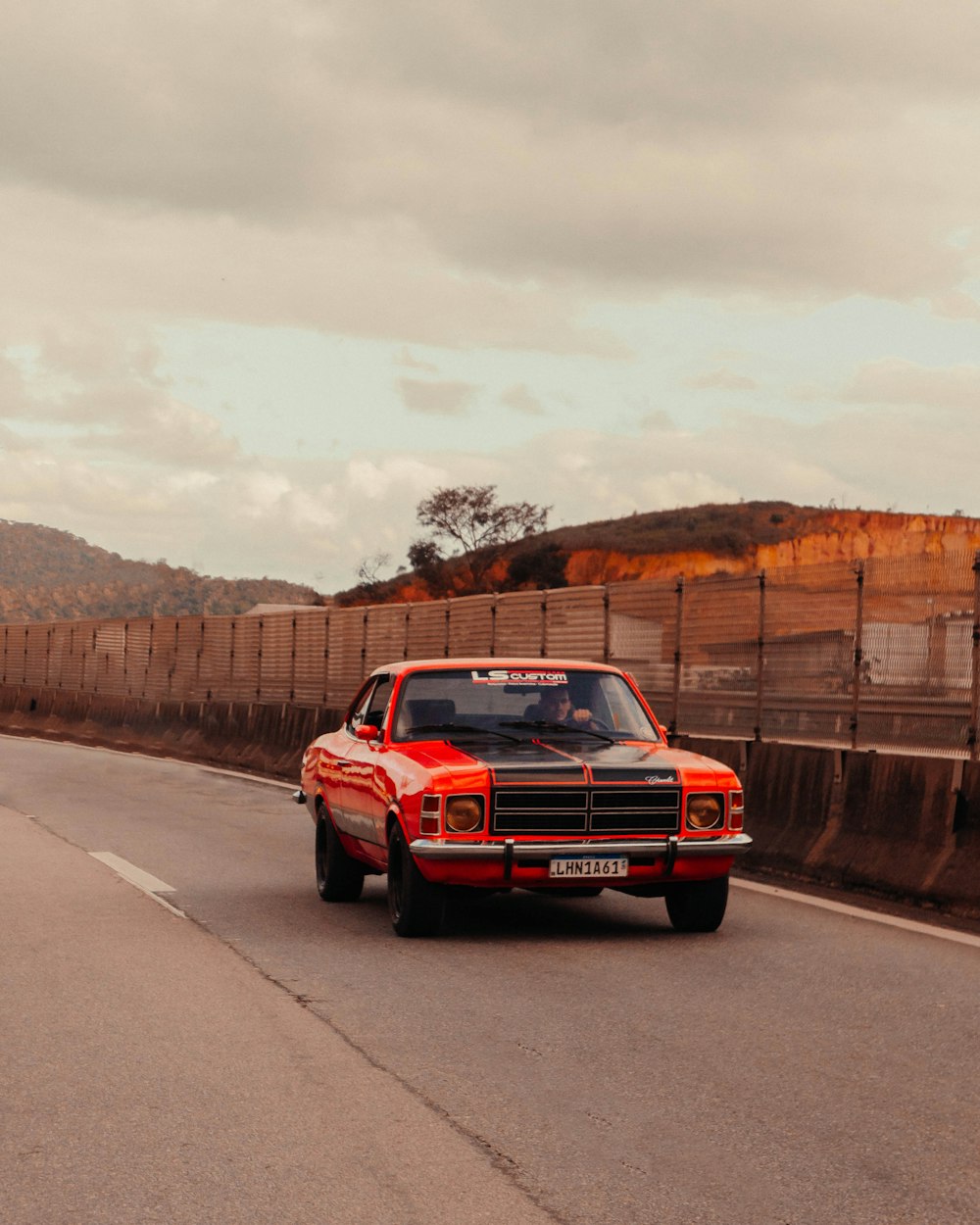 a red truck driving down a road next to a fence