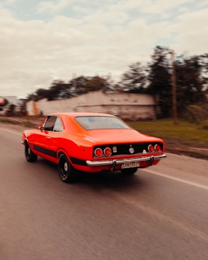 a red car driving down a road next to a forest