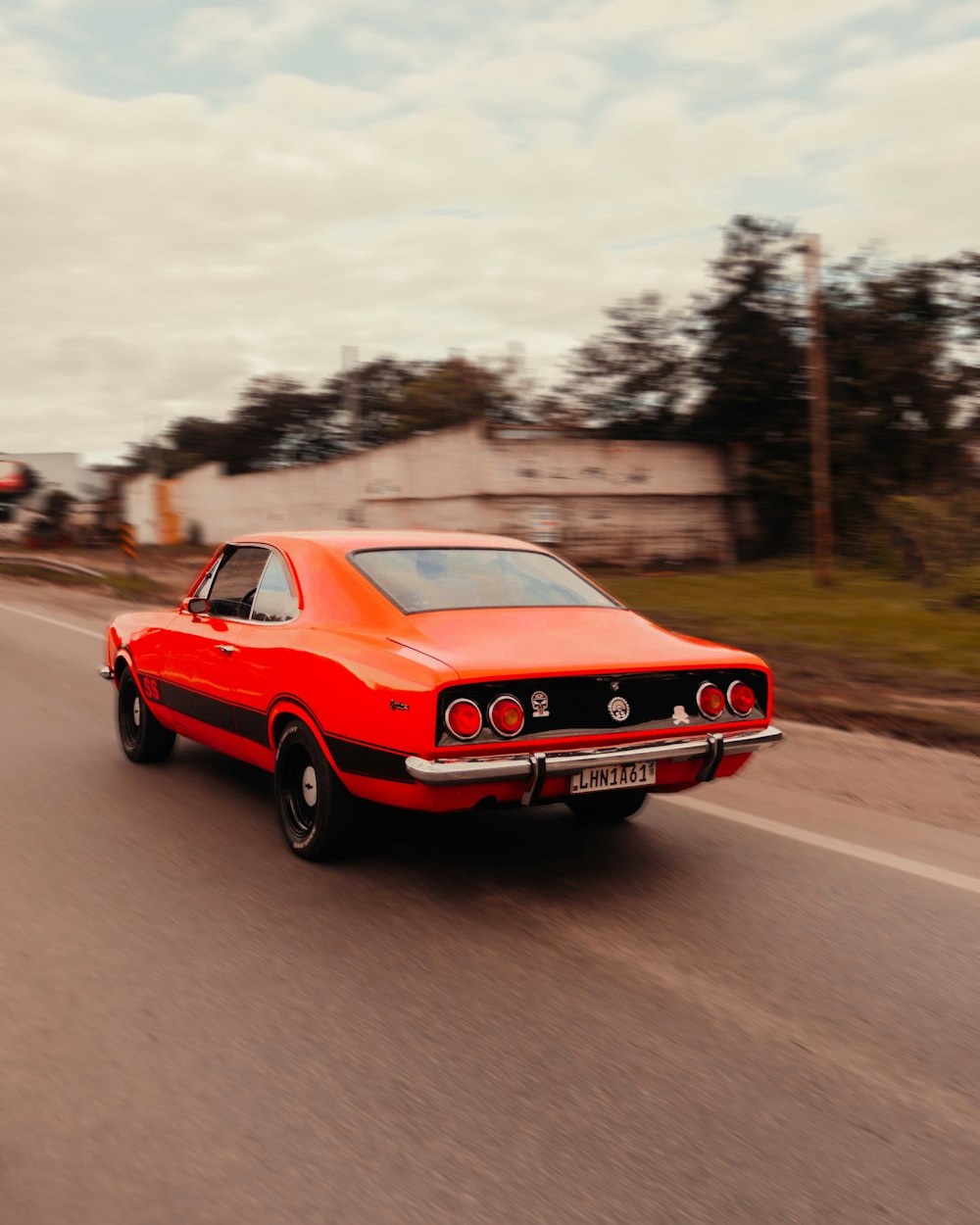 a red car driving down a road next to a forest