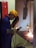 A worker engaged in welding, wearing a yellow safety helmet, protective gloves, and a face shield. Sparks are visible as the welding process takes place inside a workshop. The worker is standing at a metal workbench, carefully operating a welding tool.