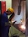 A worker engaged in welding, wearing a yellow safety helmet, protective gloves, and a face shield. Sparks are visible as the welding process takes place inside a workshop. The worker is standing at a metal workbench, carefully operating a welding tool.