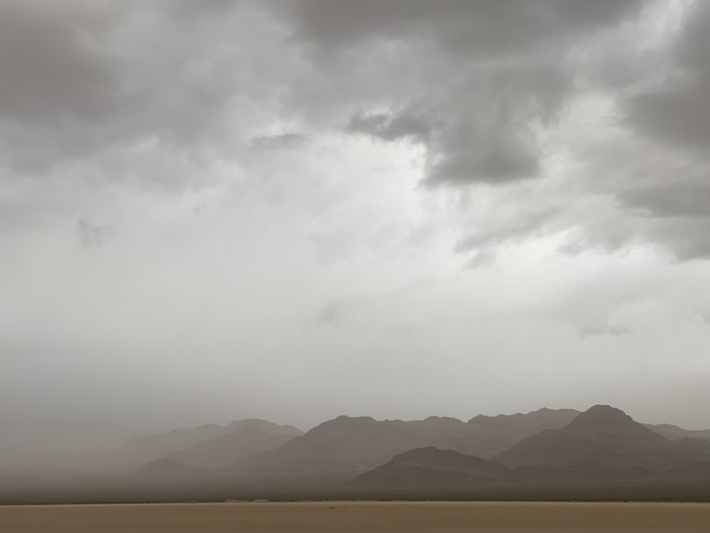 a cloudy sky over a desert landscape with mountains in the distance