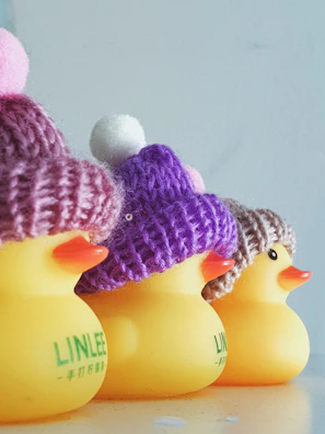 Four rubber ducks lined up on a bathroom shelf, each with different colorful sticker designs behind them.