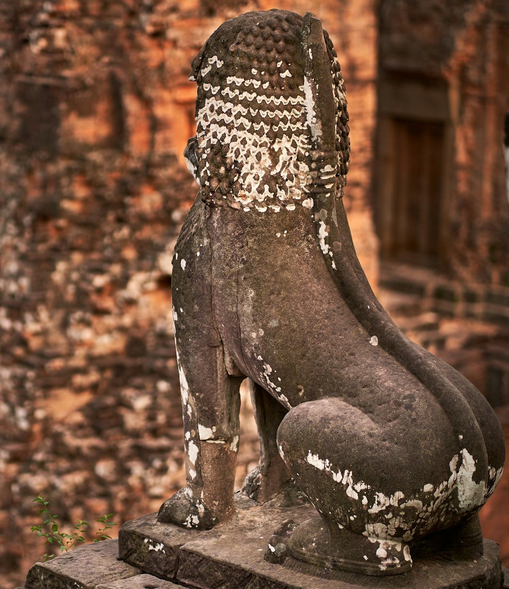 Una estatua de piedra de un perro sentado frente a una pared de ladrillo