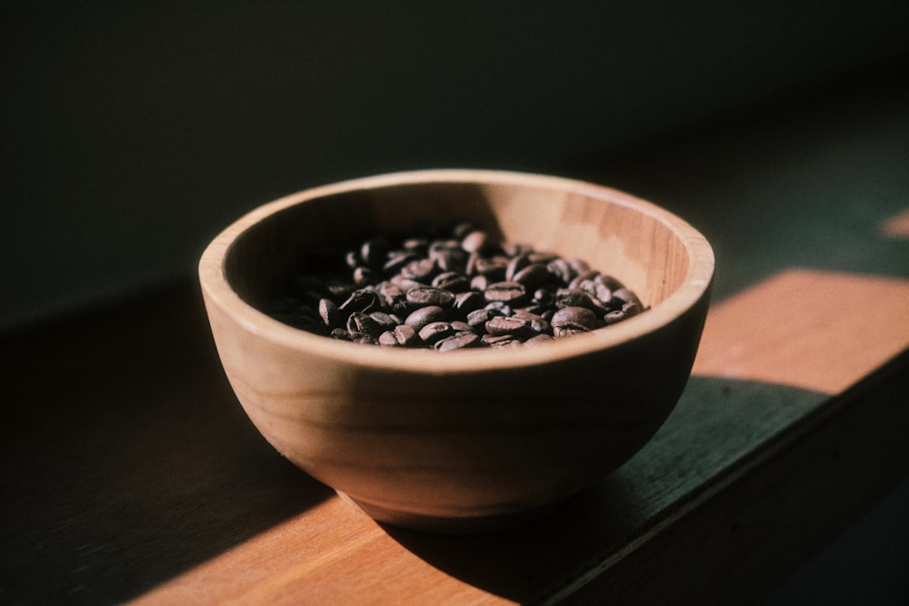 a wooden bowl filled with coffee beans on top of a table