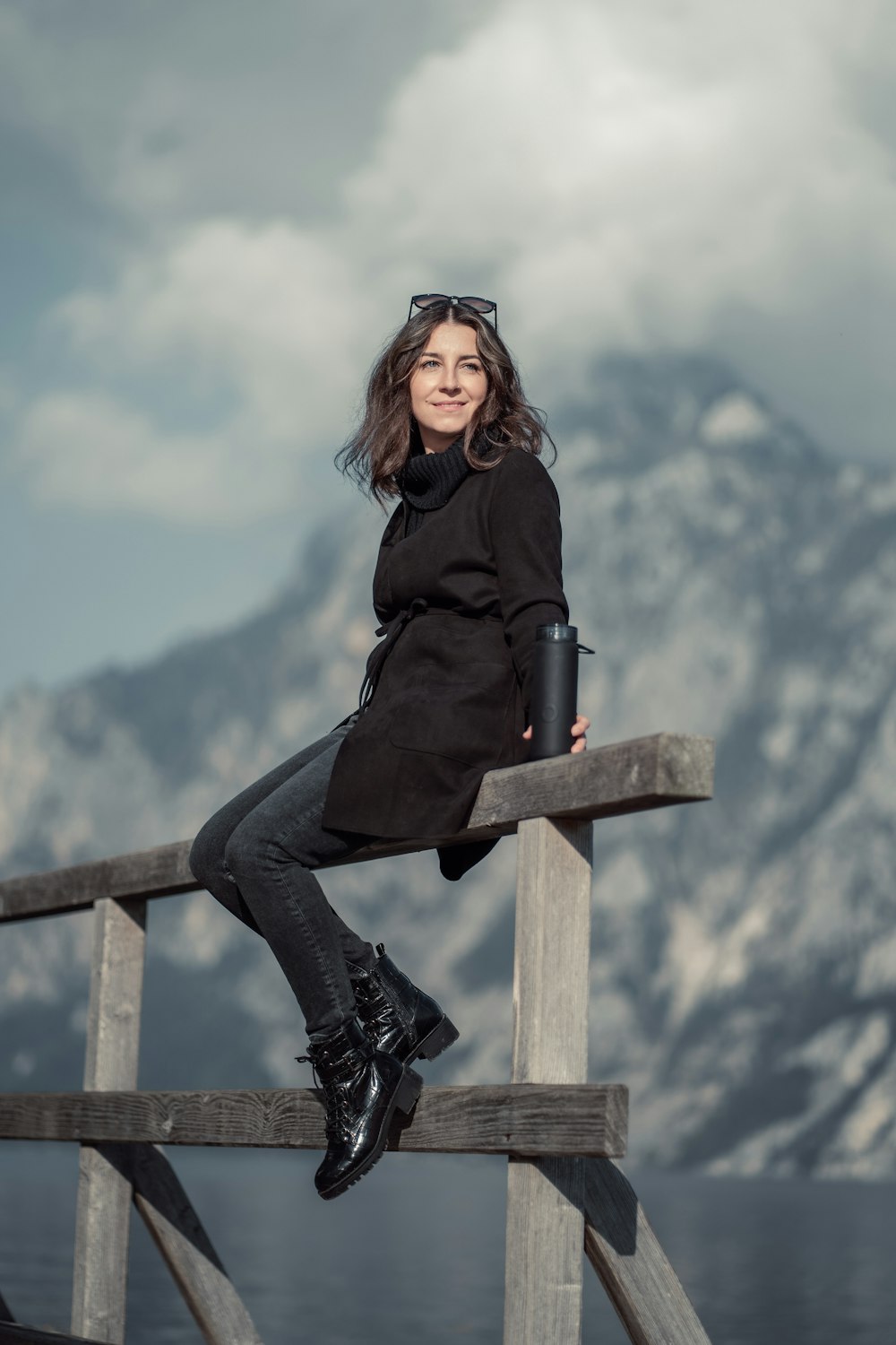 a woman sitting on a wooden rail next to a body of water