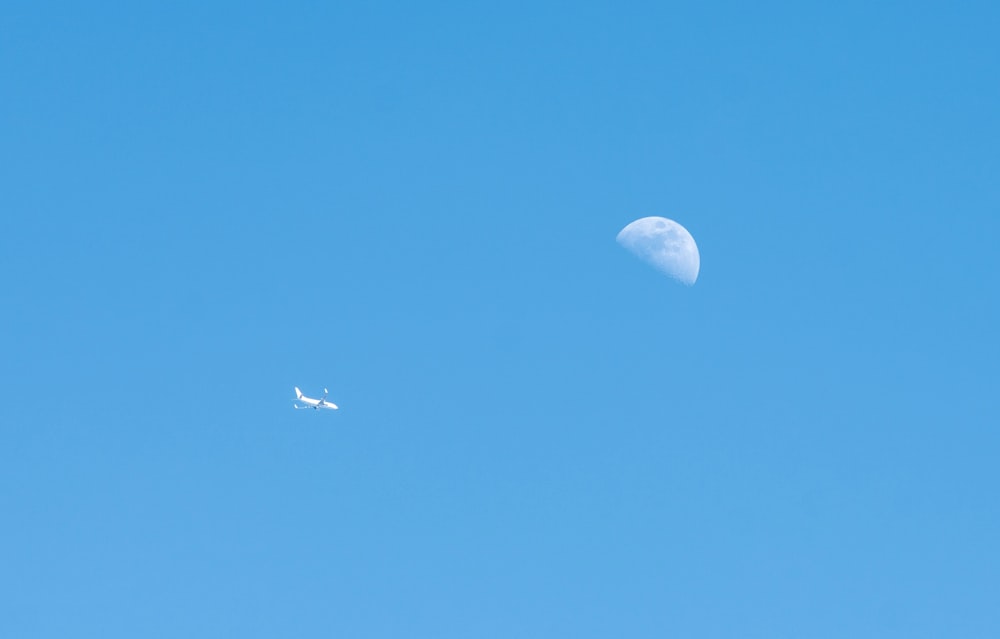 an airplane flying past a half moon in a blue sky