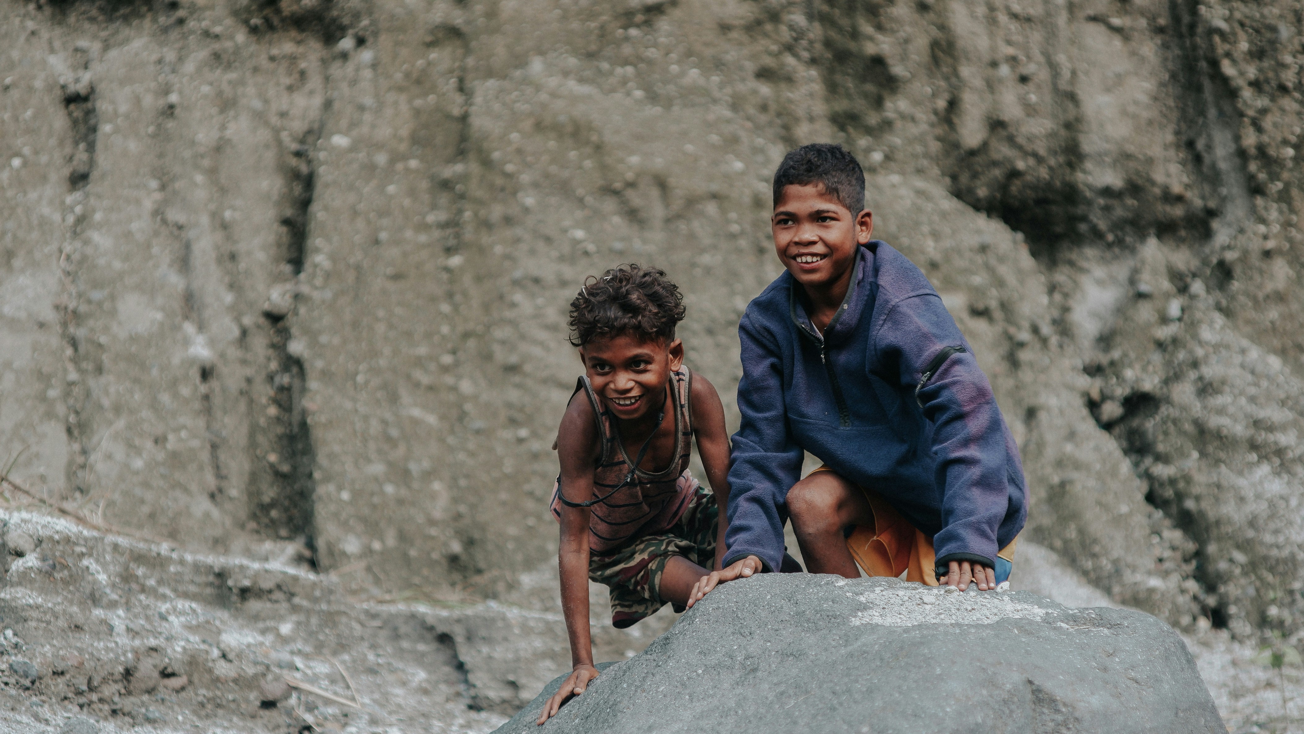 two young boys are climbing up a rock