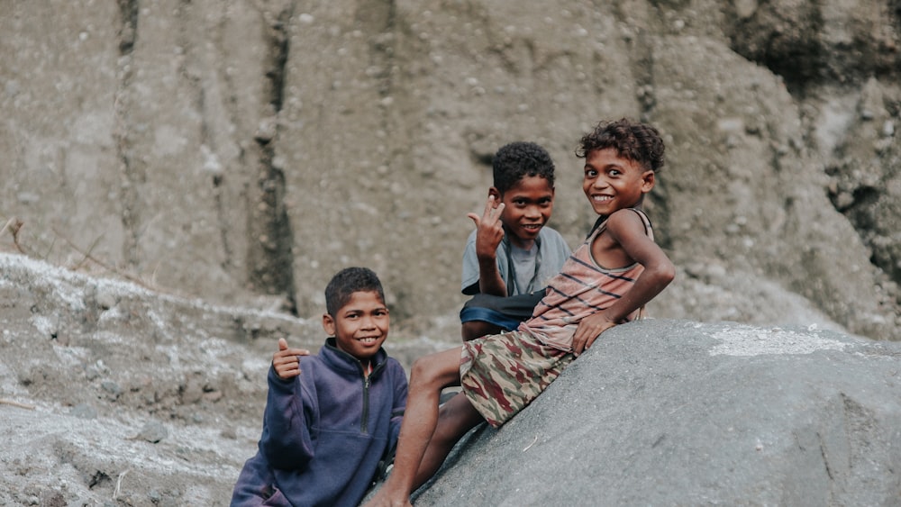 three young boys sitting on a rock in front of a mountain