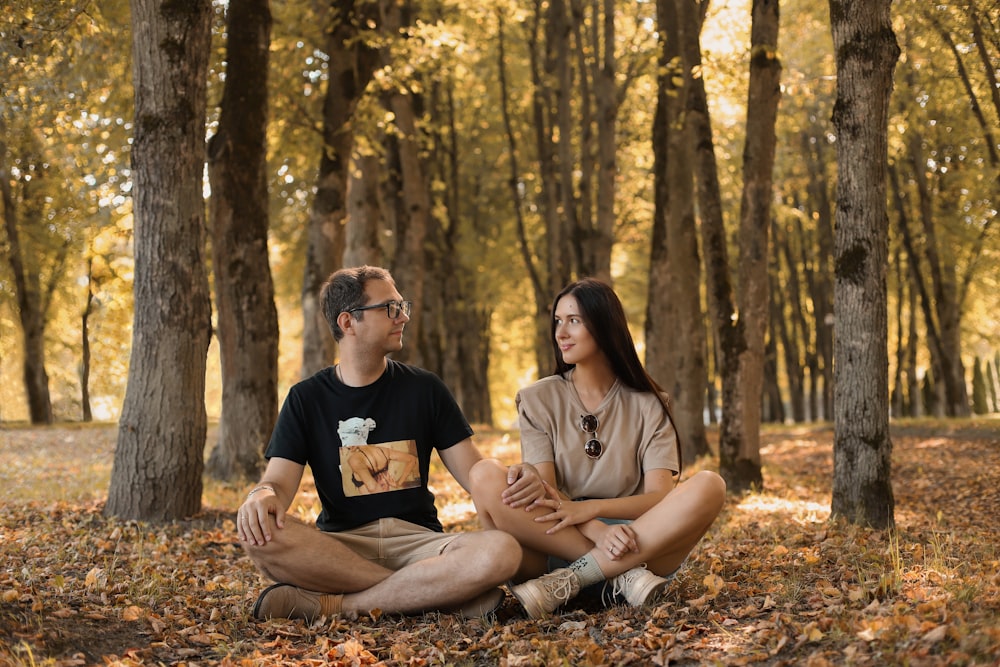 a man and a woman sitting on the ground in a forest