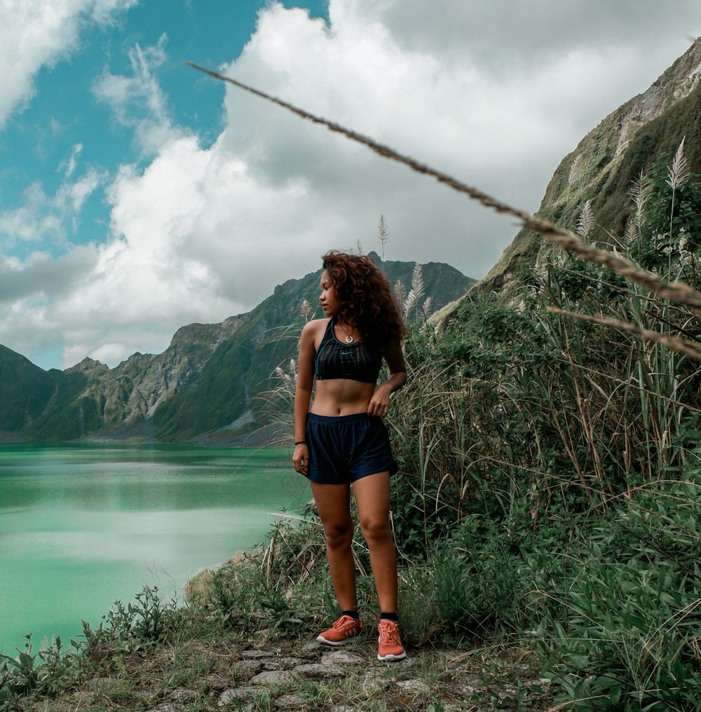 a woman in a sports bra top and shorts standing by a lake