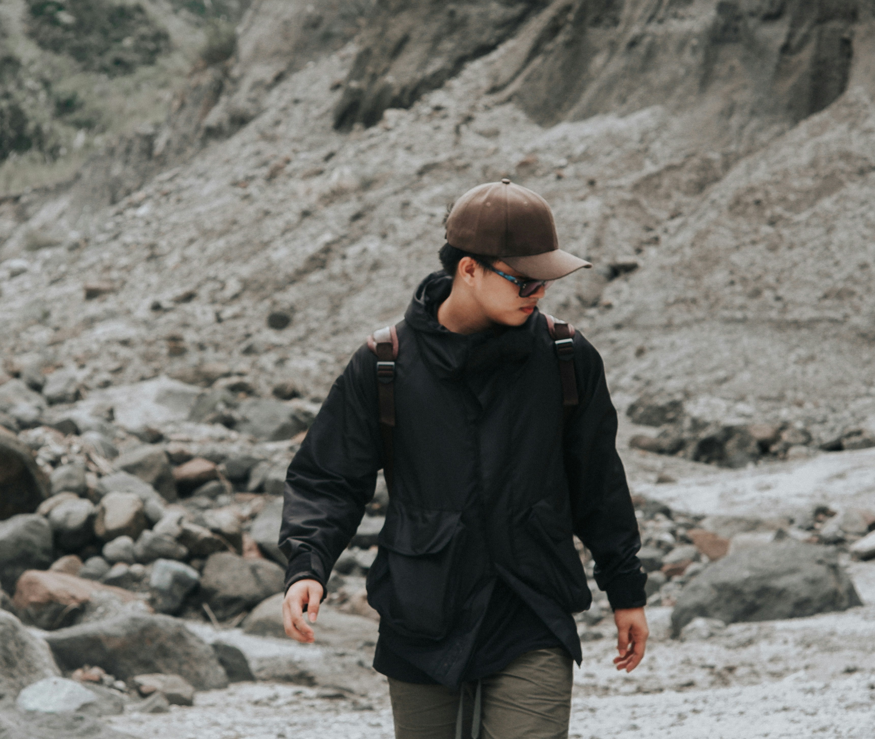 a man walking on a rocky beach with a hat on