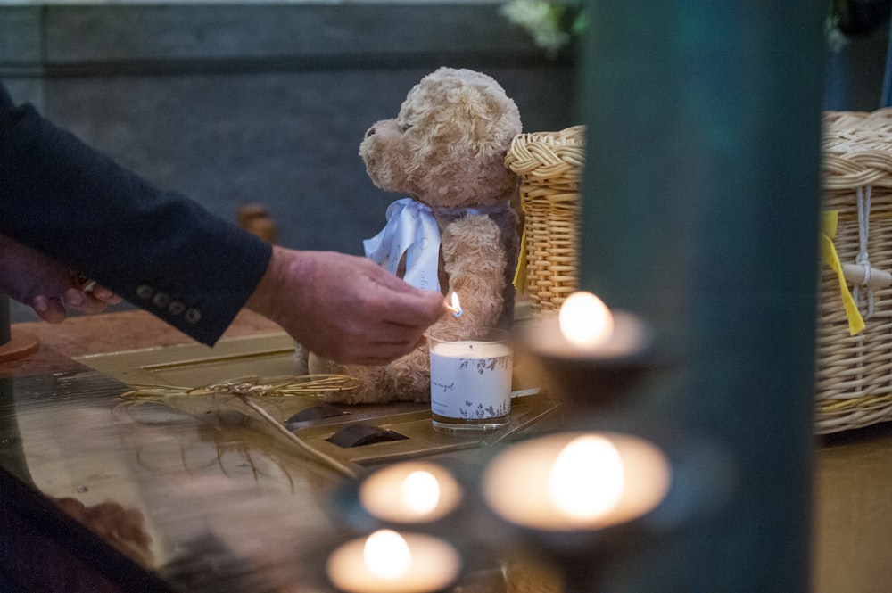 a person lighting a candle on a table with a teddy bear