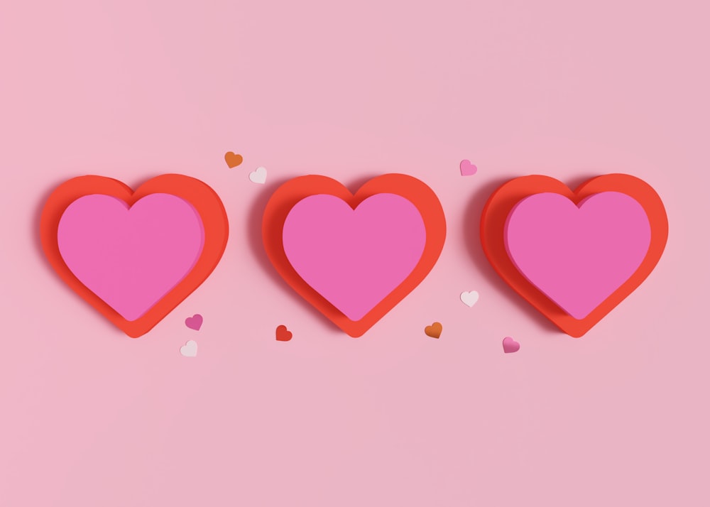 three red hearts with confetti on a pink background