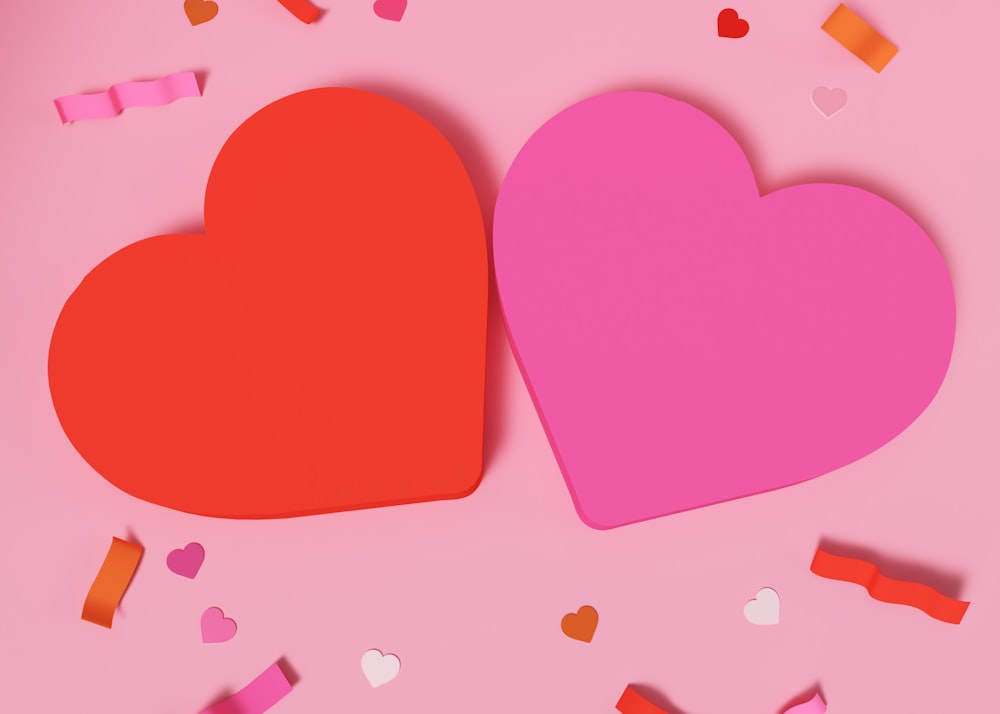 two paper hearts on a pink background surrounded by confetti