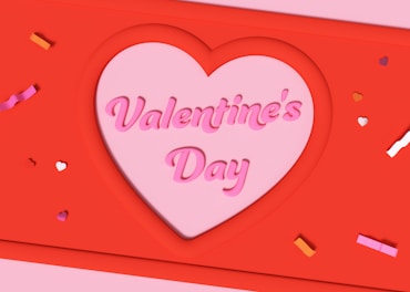 A heart-shaped cutout contains the words 'Valentine's Day' in pink, set against a vibrant red background. Small colored heart and confetti shapes are scattered around, adding a festive touch.