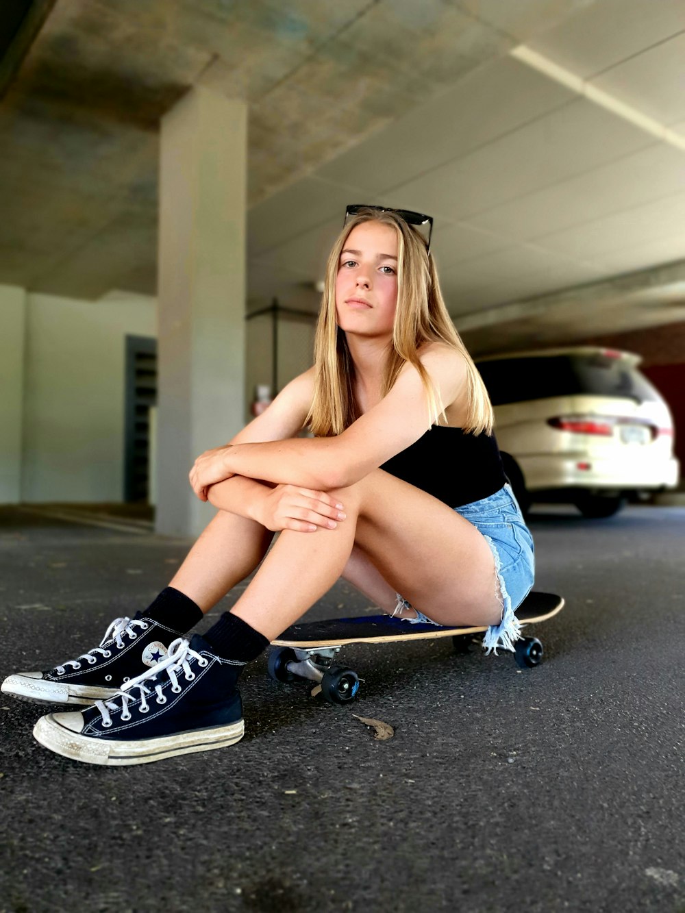 a girl sitting on a skateboard in a parking garage