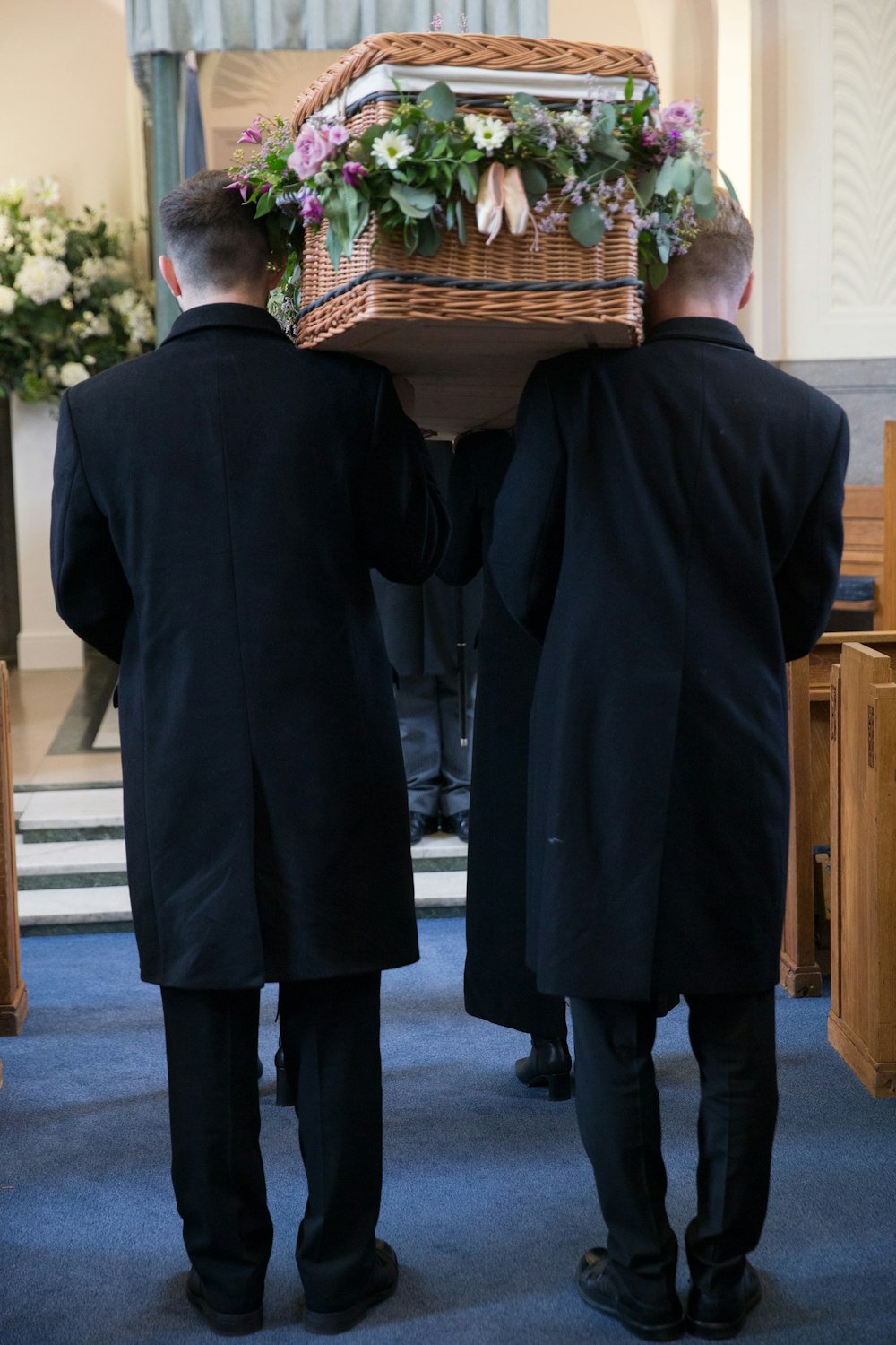 two men carrying a casket with flowers on it