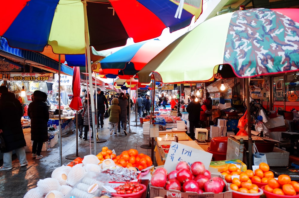 Un mercado con una variedad de frutas y verduras bajo sombrillas