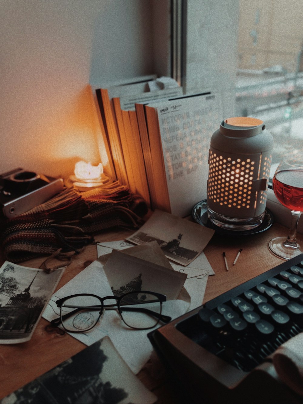 a desk with a keyboard, glasses and a lamp