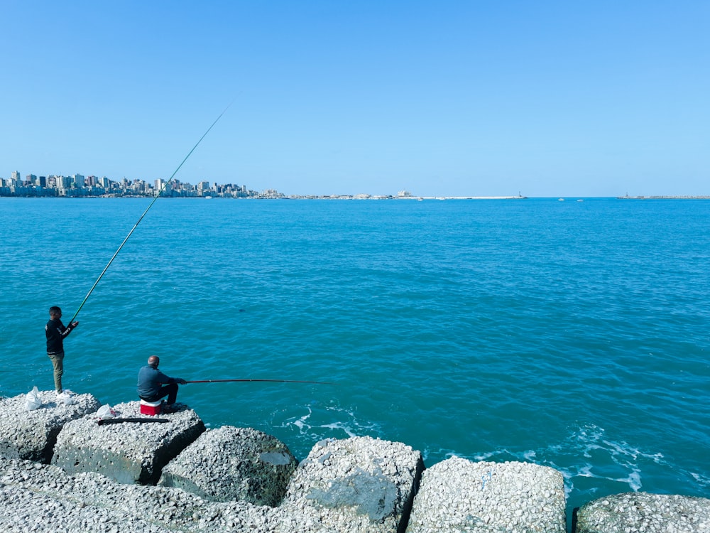 a man sitting on a rock next to a body of water