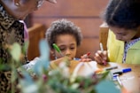 A group of children and an adult are engaged in a creative activity, drawing on a surface with colorful markers. The scene captures a warm and intimate moment of interaction and focus.