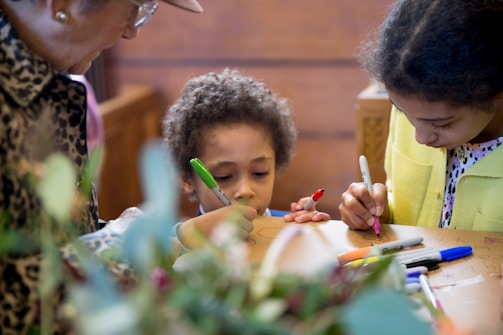 A group of children and an adult are engaged in a creative activity, drawing on a surface with colorful markers. The scene captures a warm and intimate moment of interaction and focus.