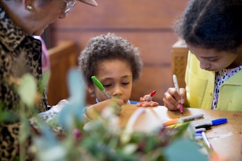 A group of children and an adult are engaged in a creative activity, drawing on a surface with colorful markers. The scene captures a warm and intimate moment of interaction and focus.