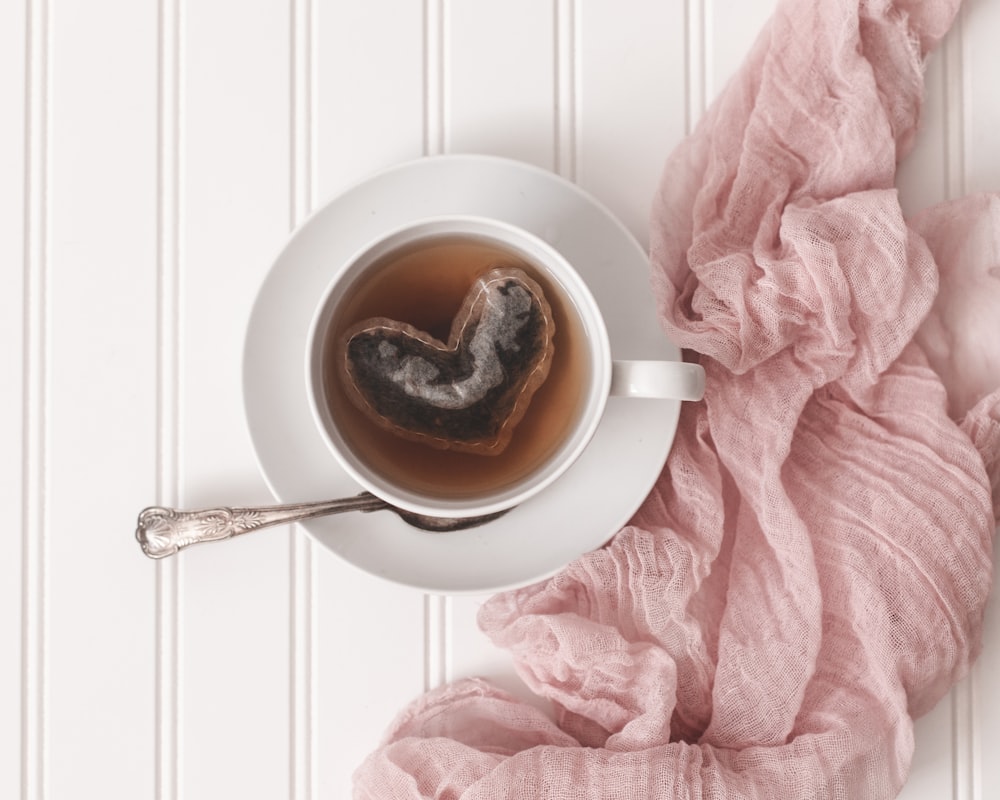 una taza de té en un platillo junto a una manta rosa