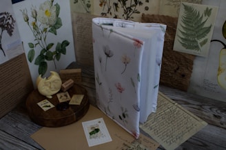 A softly lit display of botanical-themed literary replicas and stationery on a wooden table.