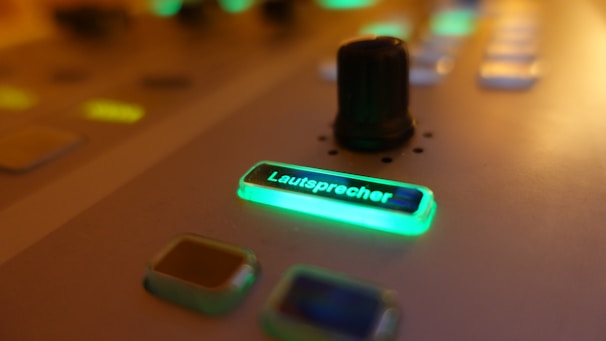 A close-up view of a control interface with glowing buttons, one of which reads 'Lautsprecher' illuminated in green, and a small black knob surrounded by softly lit buttons.