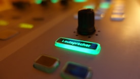 A close-up view of a control interface with glowing buttons, one of which reads 'Lautsprecher' illuminated in green, and a small black knob surrounded by softly lit buttons.