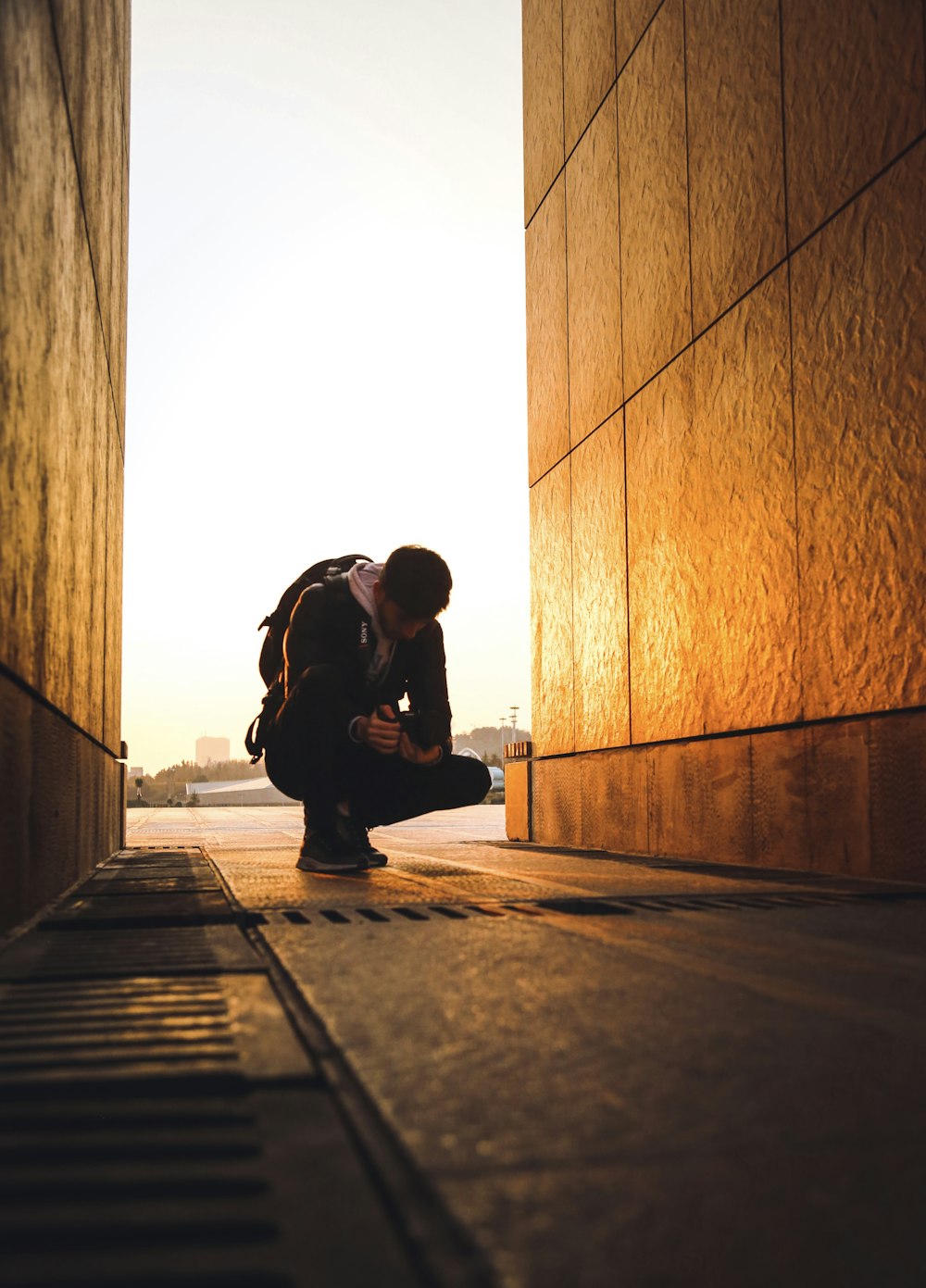a man kneeling down next to a wall looking at his cell phone